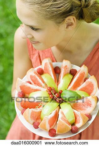 Stock Image - Woman holding plate full of fruit slices, high angle view. Fotosearch