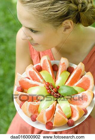 Stock Image - Woman holding plate full of fruit slices, high angle view. Fotosearch