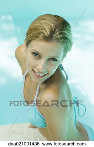 Stock Photograph - Woman in bikini smiling at camera, pushing self up on edge of pool. Fotosearch
