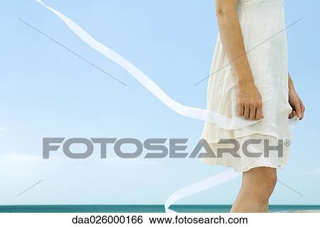 Woman in dress holding ribbon, tousled by wind, low angle view, cropped View Large Photo Image Stock Photograph - Woman in dress holding ribbon, tousled by wind, low angle view, cropped. Fotosearch