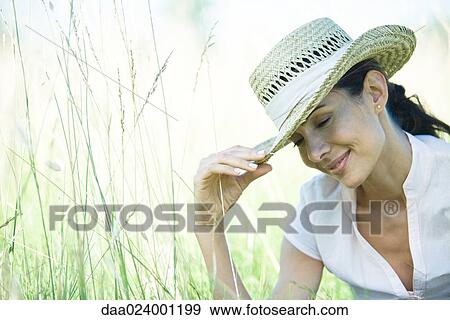 Stock Photo - Woman in field, holding edge of hat. Fotosearch