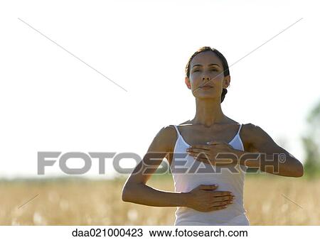 Stock Image - Woman in field, with hands on chest and stomach. Fotosearch
