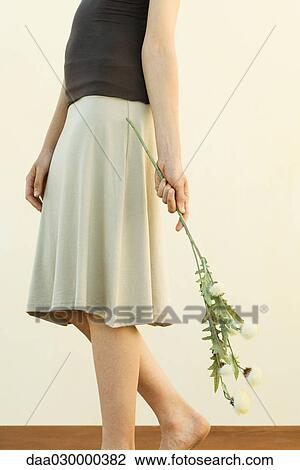 Stock Image - Woman in skirt holding flowers, cropped view. Fotosearch