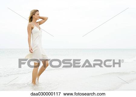 Stock Photo - Woman in sundress walking at the beach, side view. Fotosearch