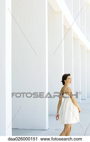 Stock Image - Woman in sundress walking outdoors, hair tousled by wind, smiling. Fotosearch