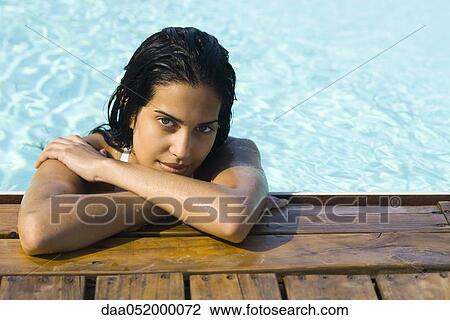 Stock Image - Woman in water resting at edge of swimming pool, portrait. Fotosearch