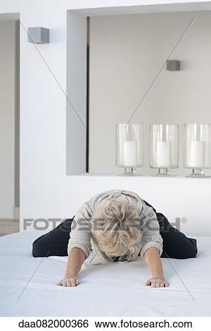 Stock Photograph - Woman kneeling on bed, leaning forward. Fotosearch