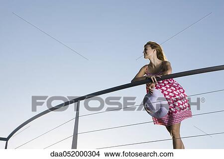 Picture - Woman leaning against balcony railing, looking at view. Fotosearch