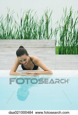 Woman leaning against edge of pool, looking at self in surface of water, lake in background View Large Photo Image Picture - Woman leaning against edge of pool, looking at self in surface of water, lake in background. Fotosearch
