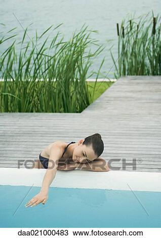 Woman leaning against edge of pool, touching surface of water, lake in background View Large Photo Image Stock Image - Woman leaning against edge of pool, touching surface of water, lake in background. Fotosearch
