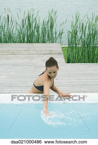 Woman leaning against edge of pool, touching surface of water, lake in background View Large Photo Image Stock Photograph - Woman leaning against edge of pool, touching surface of water, lake in background. Fotosearch