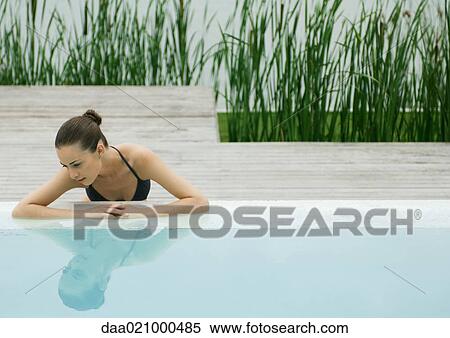 Stock Photography - Woman leaning against edge of pool, looking at self in surface of water, lake in background. Fotosearch