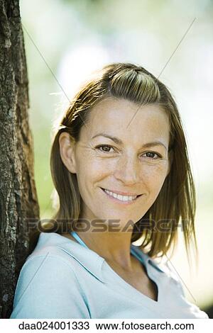 Woman leaning against tree, smiling at camera, portrait View Large Photo Image Stock Image - Woman leaning against tree, smiling at camera, portrait. Fotosearch