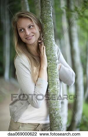 Woman leaning against tree trunk, portrait View Large Photo Image Stock Image - Woman leaning against tree trunk, portrait. Fotosearch
