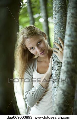 Woman leaning against tree trunk, portrait View Large Photo Image Stock Image - Woman leaning against tree trunk, portrait. Fotosearch