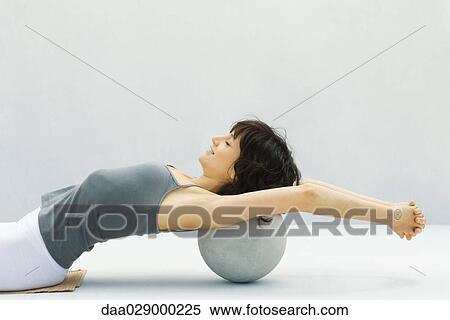 Stock Photography - Woman leaning back against fitness ball, arms outstretched, side view. Fotosearch
