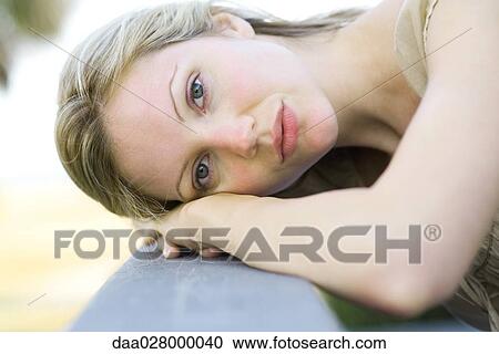 Stock Image - Woman leaning head against railing, looking at camera. Fotosearch
