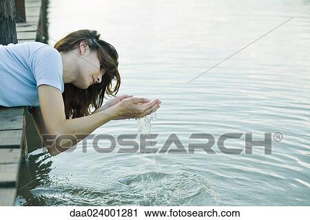 Woman leaning off edge of dock, letting water run through hands View Large Photo Image Stock Image - Woman leaning off edge of dock, letting water run through hands. Fotosearch
