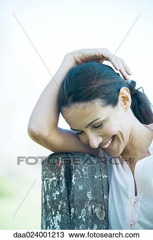 Woman leaning on wooden post, smiling, looking down View Large Photo Image Stock Image - Woman leaning on wooden post, smiling, looking down. Fotosearch