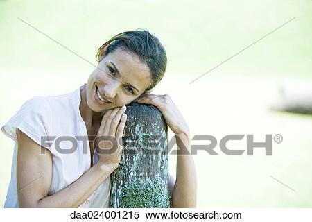Woman leaning on wooden post, smiling View Large Photo Image Stock Photography - Woman leaning on wooden post, smiling. Fotosearch
