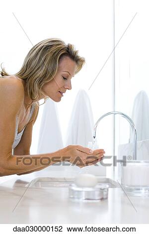 Woman leaning over bathroom sink, holding hands under running water View Large Photo Image Stock Image - Woman leaning over bathroom sink, holding hands under running water. Fotosearch