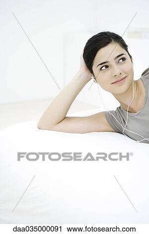 Woman listening to earphones, reclining on mattress, looking away View Large Photo Image Stock Image - Woman listening to earphones, reclining on mattress, looking away. Fotosearch