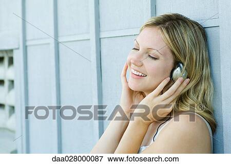 Stock Photo - Woman listening to earphones, smiling. Fotosearch