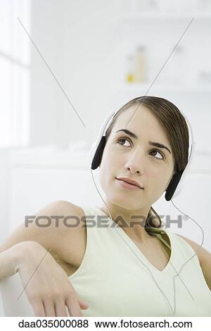 Stock Photo - Woman listening to headphones, looking up and away. Fotosearch