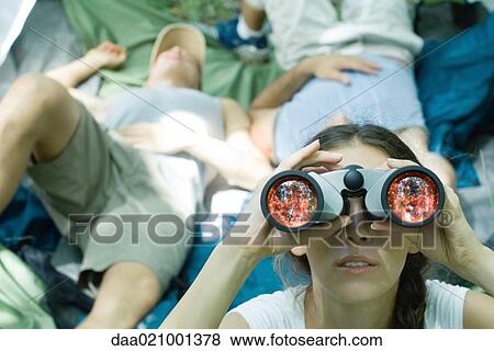 Woman looking through binoculars while friends rest in background View Large Photo Image Stock Photo - Woman looking through binoculars while friends rest in background. Fotosearch