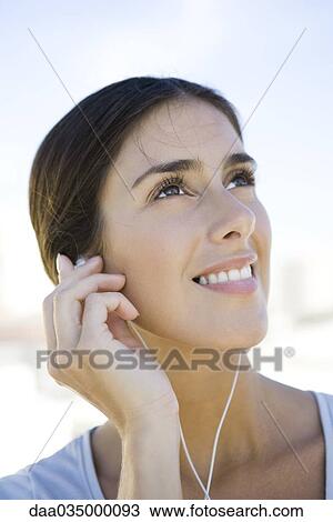 Stock Image - Woman looking up, listening to earphones. Fotosearch