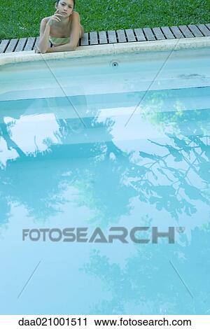 Stock Image - Woman lying by pool, looking at camera. Fotosearch