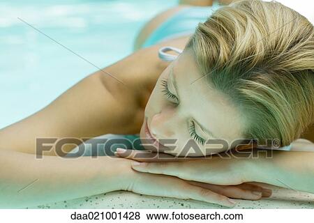 Stock Photo - Woman lying by pool, resting head on hands. Fotosearch