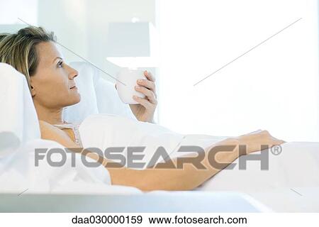 Woman lying in comfortable bed, holding mug, side view View Large Photo Image Stock Photo - Woman lying in comfortable bed, holding mug, side view. Fotosearch