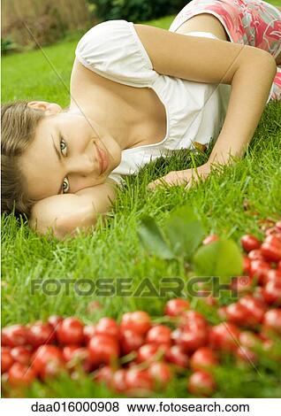 Stock Photo - Woman lying in grass, cherries in foreground. Fotosearch