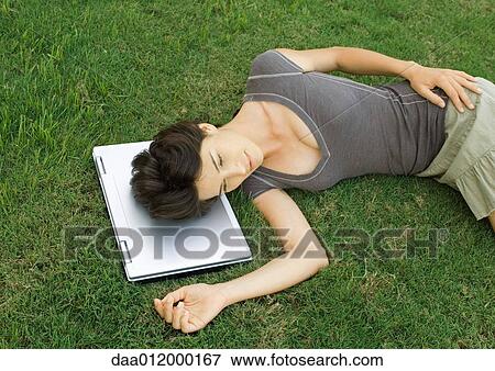 Stock Photo - Woman lying in grass, head resting on laptop computer. Fotosearch