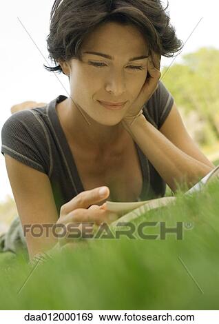 Woman lying in grass, reading book View Large Photo Image Stock Photo - Woman lying in grass, reading book. Fotosearch