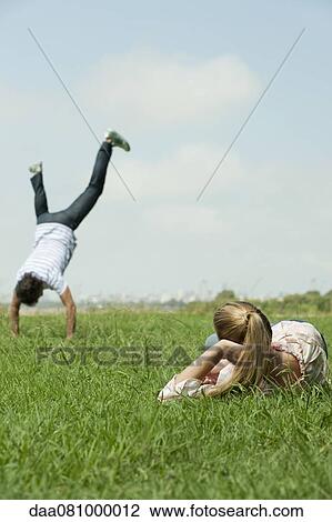 Woman lying in grass, watching man do handstand View Large Photo Image Stock Image - Woman lying in grass, watching man do handstand. Fotosearch