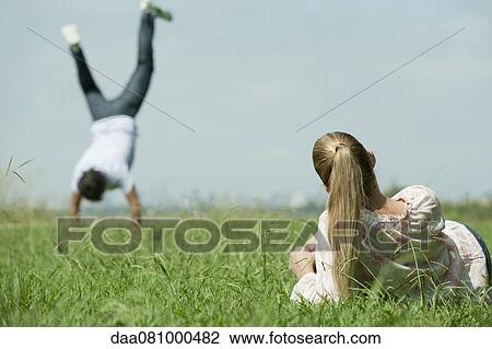 Woman lying in grass, watching man do handstand View Large Photo Image Stock Image - Woman lying in grass, watching man do handstand. Fotosearch