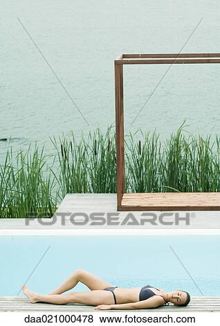 Woman lying on deck near pool, lake in background View Large Photo Image Stock Photo - Woman lying on deck near pool, lake in background. Fotosearch