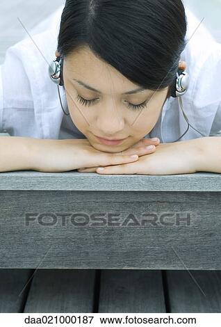 Stock Photo - Woman lying on decking listening to headphones. Fotosearch