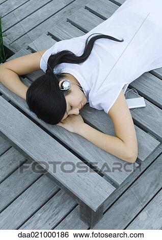 Woman lying on decking listening to headphones View Large Photo Image Stock Photograph - Woman lying on decking listening to headphones. Fotosearch