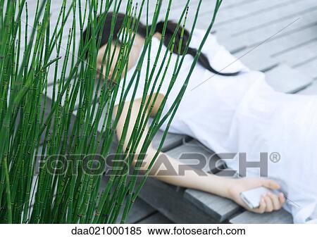 Stock Photography - Woman lying on decking listening to headphones. Fotosearch