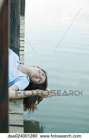 Stock Image - Woman lying on dock with head hanging off edge, smiling. Fotosearch