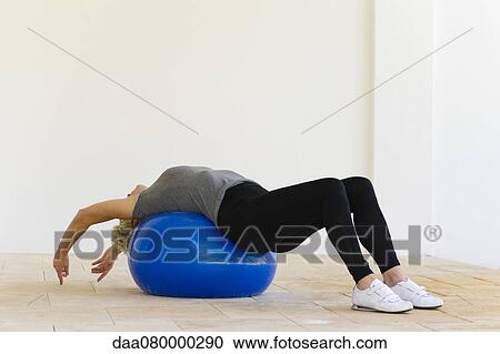 Stock Image - Woman lying on fitness ball stretching. Fotosearch