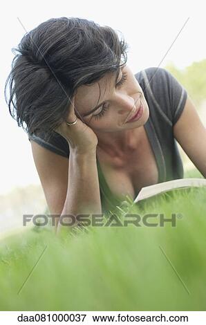 Stock Photo - Woman lying on grass reading book. Fotosearch