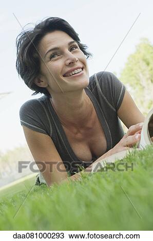 Woman lying on grass with book, smiling View Large Photo Image Stock Image - Woman lying on grass with book, smiling. Fotosearch