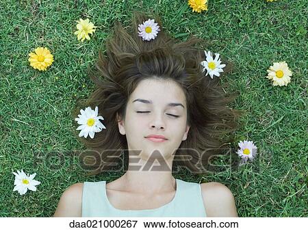 Stock Photo - Woman lying on grass with flowers scattered around head, eyes closed. Fotosearch
