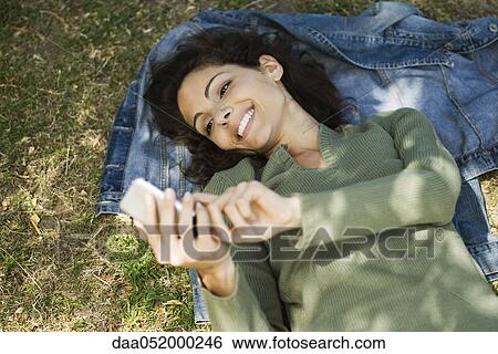 Stock Photograph - Woman lying on ground text messaging. Fotosearch