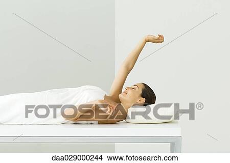 Woman lying on massage table, eyes closed, one arm raised View Large Photo Image Picture - Woman lying on massage table, eyes closed, one arm raised. Fotosearch