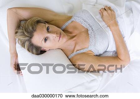 Stock Image - Woman lying on pillow, smiling at camera. Fotosearch